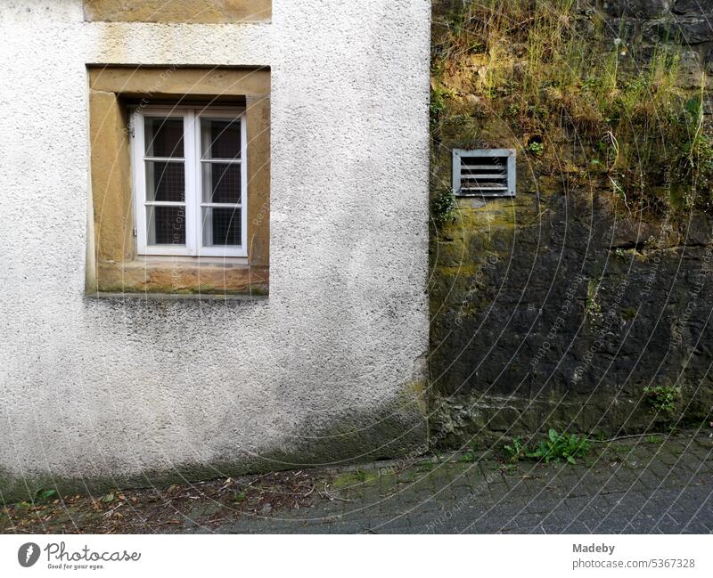 Verwaschene alte Fassade in Pastellfarben mit weißem Sprossenfenster aus Holz und Rahmen aus Naturstein in der Altstadt von Oerlinghausen bei Bielefeld am Hermannsweg im Teutoburger Wald in Ostwestfalen-Lippe