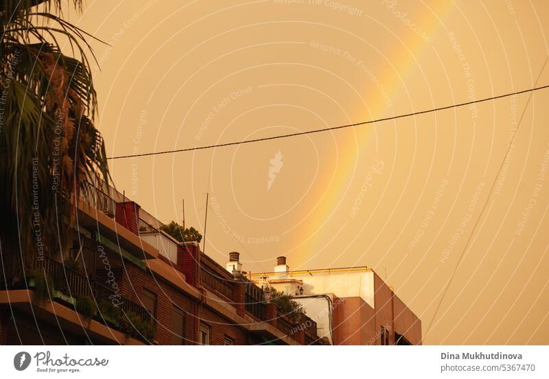 Regenbogen am Himmel während des Sturms und Regens. Orange stürmischer Himmel. Schlechtes Wetter tropischer Sturm. farbenfroh Großstadt Unwetter Wahrzeichen