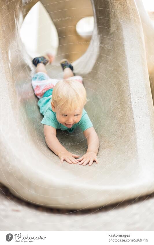 Kind spielt auf Spielplatz im Freien. Kleinkind spielt auf Schule oder Kindergarten Hof. Aktives Kind auf Stein gemeißelter Rutsche. Gesunde Sommeraktivität für Kinder. Kleiner Junge klettert im Freien.