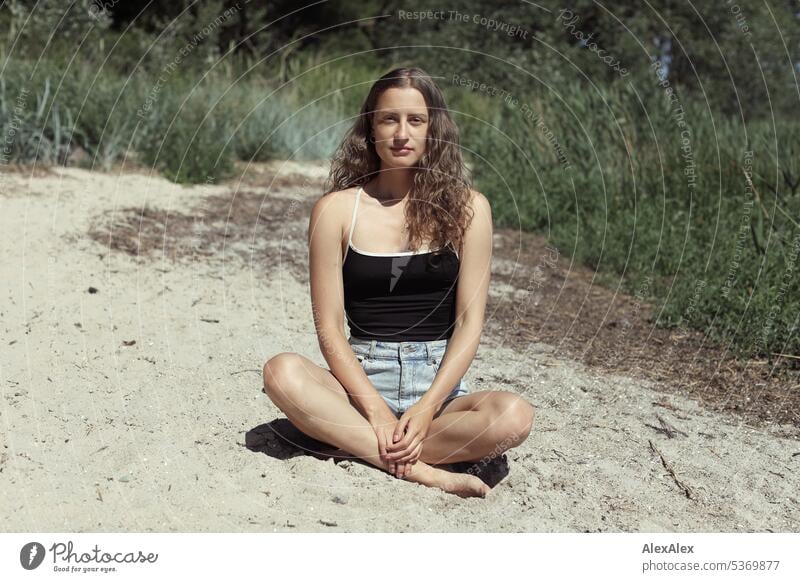 direktes Portrait einer schönen, schlanken, brünetten, jungen Frau vor einem Wald im Sommer junge Frau langhaarig Locken fit gutaussehend natürlich ästhetisch