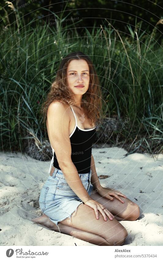 seitliches Portrait einer jungen, schönen, brünetten Frau, die im Sand vor einem Wald kniet warm sommerlich schönes wetter Sommer Pflanzen Nähe Tag Ruhe