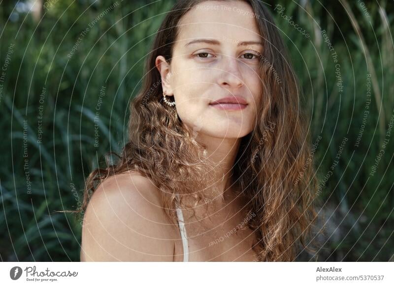 direktes Portrait einer jungen, schönen, brünetten, Frau, die im Sand vor einem Wald sitzt warm sommerlich schönes wetter Sommer Pflanzen Nähe Tag Ruhe