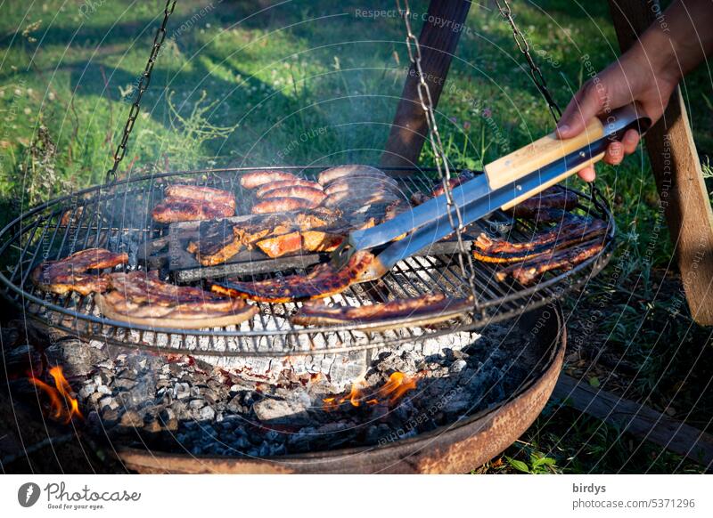 Fleisch und Würste grillen über offenem Feuer Grillen Grillrost Grillsaison Feuerschale Ernährung Glut Rauch Sommer lecker heiß Fleisch wenden Grillzange Garten