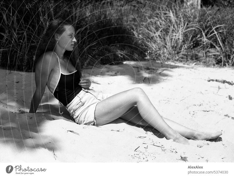 analoges, schwarzweißes, seitliches Ganzkörper- Portrait einer jungen, schönen Frau am Strand warm sommerlich schönes wetter Sommer Tag Selbstbewußt