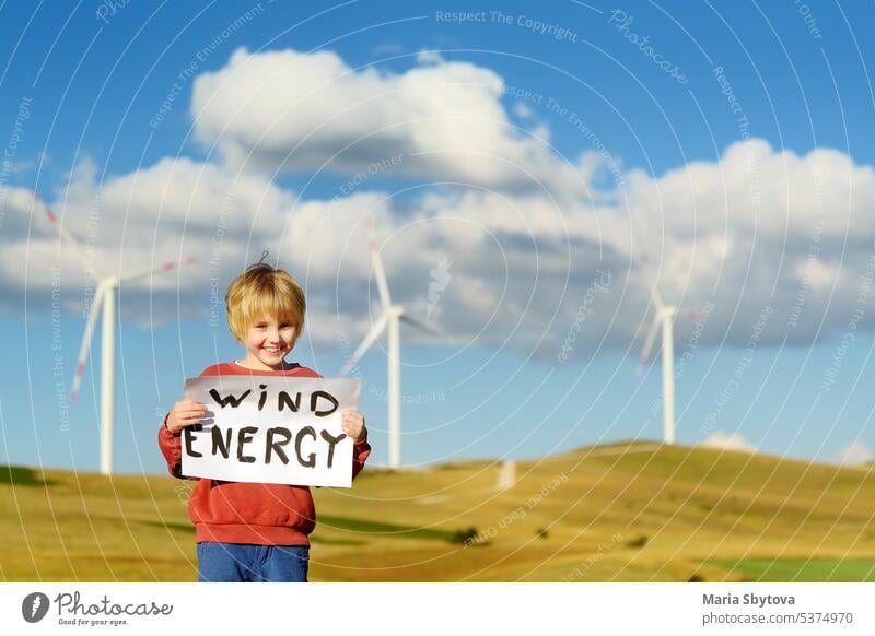 Öko-Aktivist Junge mit Banner "Windenergie" auf dem Hintergrund von Kraftwerken für erneuerbare elektrische Energieerzeugung. Kind und Windmühlen. Windturbinen zur Stromerzeugung. Grüne Energie