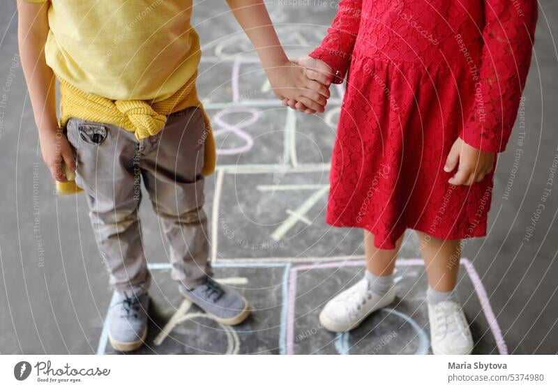 Kleiner Junge und Mädchen auf Hintergrund hopscotch die auf Asphalt gezeichnet. Kinder spielen hop scotch Spiel auf dem Spielplatz im Freien an einem sonnigen Tag. Kinder haben Spaß. Beste Freunde