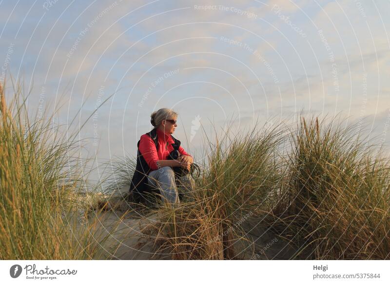 Señora sitzt in der Abendsonne im Dünengras und schaut aufs Meer Frau Mensch Seniorin Sonnenlicht sitzen schauen genießen Himmel Wolken schönes Wetter Insel