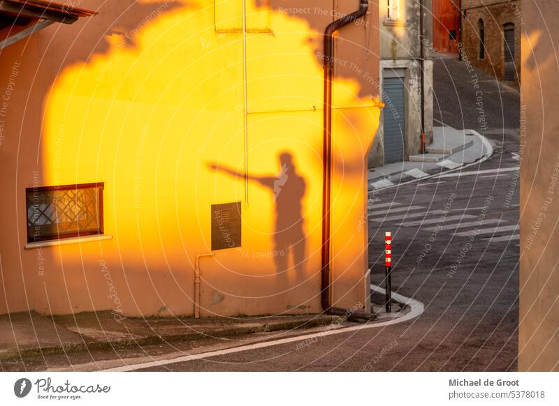 Schatten eines zeigenden Mannes auf einer orangefarbenen Wand in der Via Colle S. Francesco in der Gemeinde Cossignano in der Provinz Ascoli Piceno in Italien.