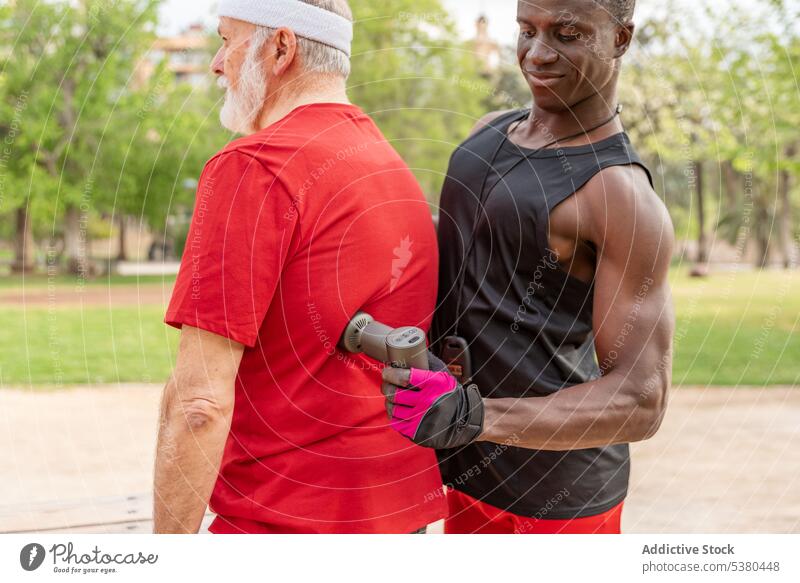 Fit schwarzer Trainer massiert den Rücken eines älteren Kunden mit einem Gerät im Park Männer Massage Trainerin Training Massagegerät Klient Wellness