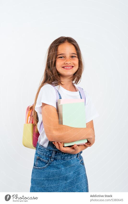 Fröhliches Schulmädchen mit Rucksack Mädchen Lächeln Schule positiv Schüler Kind Bildung Glück Notebook Pupille Jeansstoff führen wenig froh Studioaufnahme