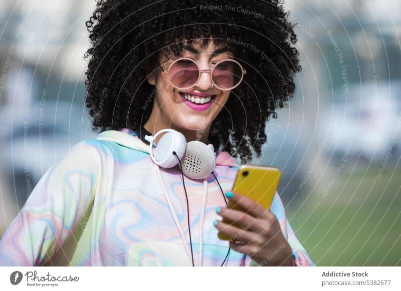 Fröhliche ethnische Frau mit Smartphone Glück heiter Sportpark Zaun Moment Sommerzeit jung hispanisch positiv Sonnenlicht Mobile Telefon Apparatur Gerät