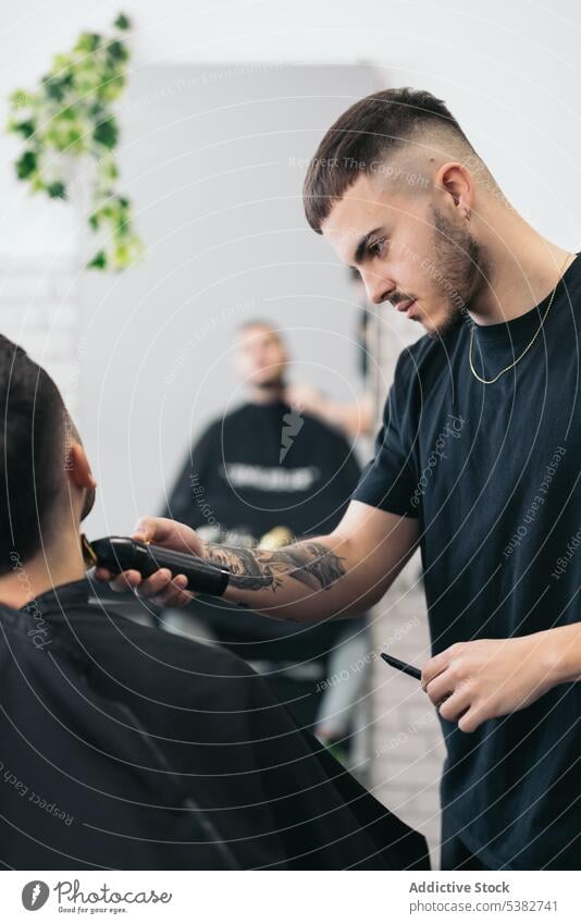 Junger Friseur schneidet Bart im Friseursalon Barbershop Vollbart bärtig Bartiger Mann Schönheit Klinge Pflege Klient Ausschnitt Frisur Kamm Kutter Schneiden