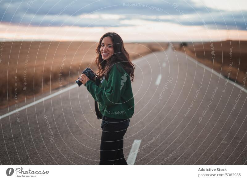 Junge Frau mit Fotokamera auf der Straße stehend Fotoapparat Fotograf Natur Lächeln Gerät Fotografie fotografieren positiv jung Hobby Landschaft lässig Asphalt