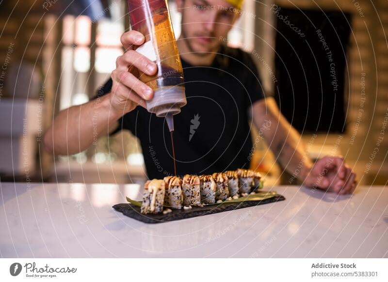 Seriöser junger Mann, der Soße auf Gunkan Maki gibt Koch maki Konzentration lecker Garnierung geschmackvoll Abfertigungsschalter Sushi vorbereiten Küche