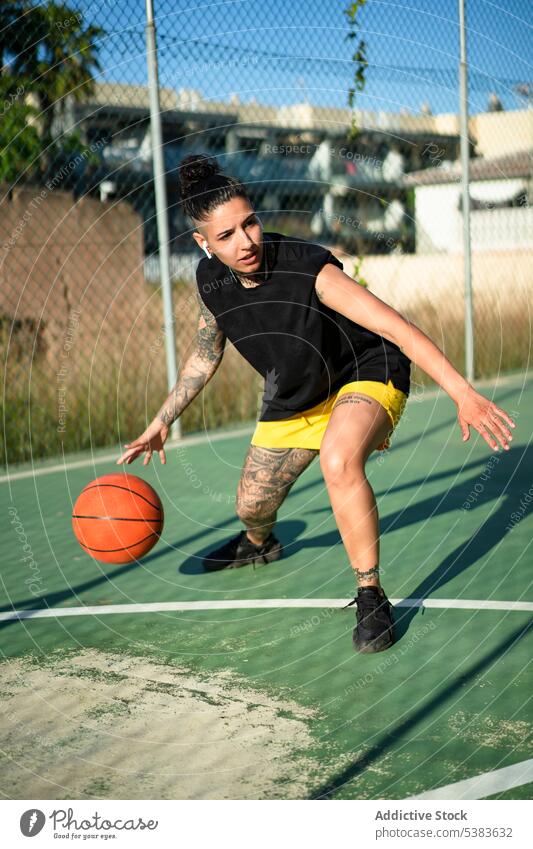 Brutale Frau dribbelt Basketball auf dem Platz Sportlerin Spieler dribbeln Sportpark Ball spielen Streetball Gericht androgyn brutal Tattoo maskulin Spielplatz