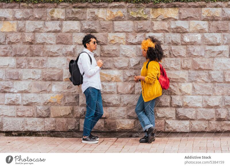 Junge Freunde mit Rucksäcken im Gespräch an einer Steinmauer Sitzung Straße Talkrunde urban modern Zusammensein reden Rucksack Freundschaft Steinwand