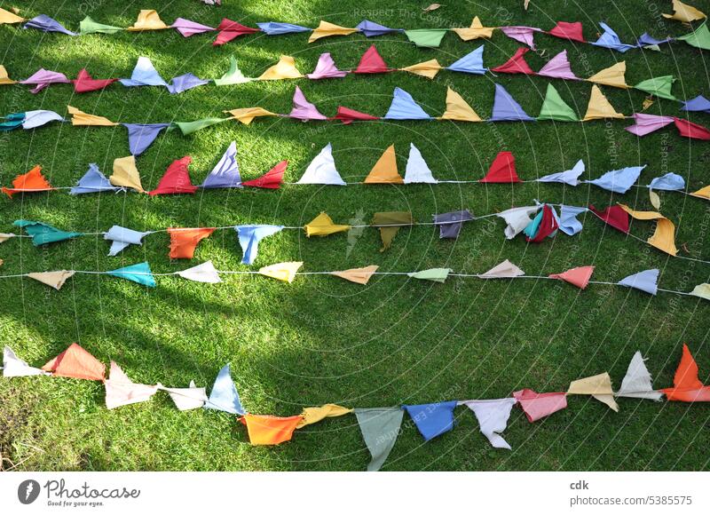 Kunterbunt: die selbstgemachte Wimpel-Girlande vom Sommerfest trocknet nach dem Regen auf der Wiese in der Sonne. Fähnchen Dekoration & Verzierung