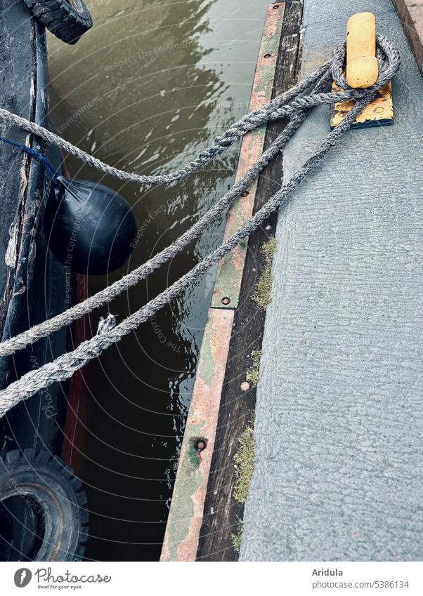 Boot mit Fender und Autoreifen an Steuerbord mit Leinen am gelben Poller festgemacht Kutter Steg Hafen Wasser Seil alt Hamburg Schifffahrt maritim Knoten