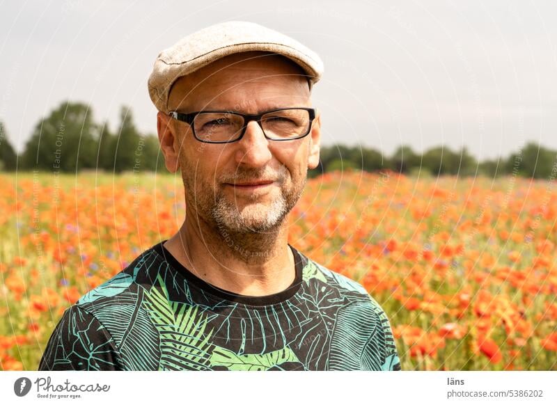 Mann im Mohn Gesicht Blick in die Kamera Landschaft Mohnblumenfeld Erwachsene Mensch Porträt Dreitagebart Brille Mütze