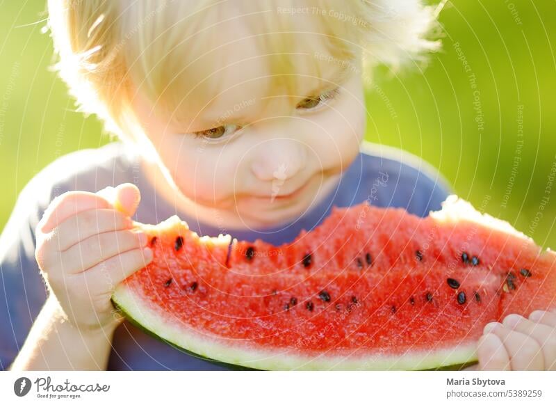 Süßer kaukasischer kleiner Junge mit blonden Haaren isst frische Wassermelone im Freien Kind Lebensmittel genießen Menschen essen Sommer Natur Mädchen weiß