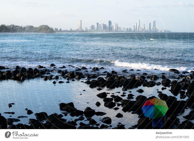 Die Große Stadt am Meer und im Vordergrund ein bunter Regenschirm zwischen den Felsen. stadt am meer Strand Ferien & Urlaub & Reisen Außenaufnahme Farbfoto