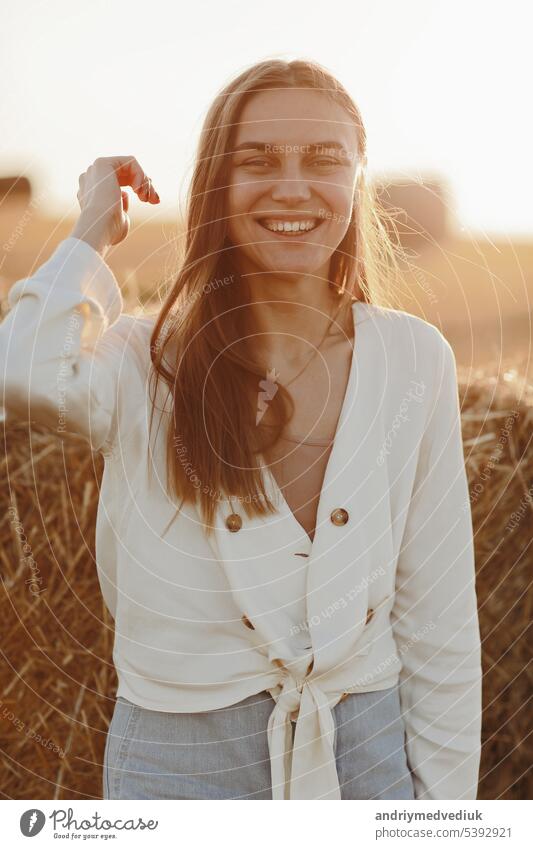 Porträt eines lächelnden schönen Mädchens mit langen Haaren in einem Jeansrock. Frau, die einen Spaziergang in einem Weizenfeld mit Heuballen an einem sonnigen Sommertag genießt.