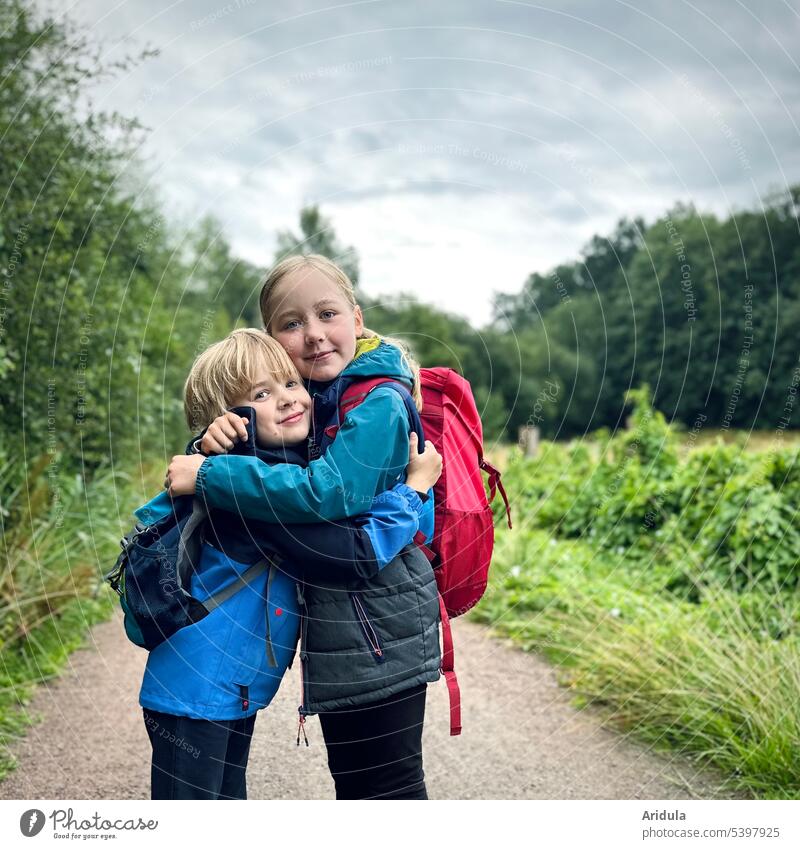 Geschwisterliebe Kinder Umarmung Junge Mädchen Blick in die Kamera Lächeln Bruder Schwester draußen wandern Rucksack Ferien & Urlaub & Reisen Kindheit Glück