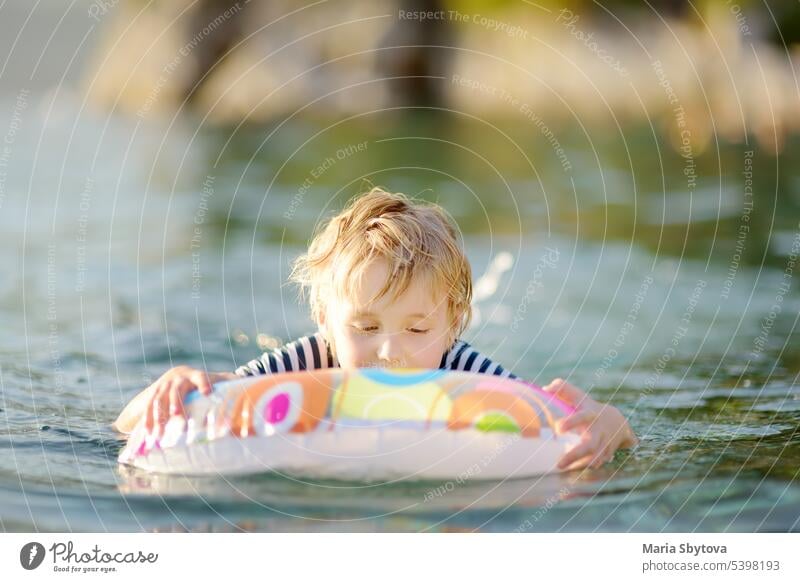 Kleiner Junge schwimmen mit bunten schwimmenden Ring im Meer auf sonnigen Sommertag. Nettes Kind spielt in sauberem Wasser. Familie und Kinder Resort Urlaub während der Sommerferien.