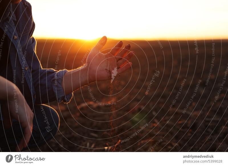 Ein männlicher Landwirt hält eine Handvoll trockenen Bodens und prüft die Fruchtbarkeit und Qualität des Bodens vor der Aussaat auf einem gepflügten Feld bei Sonnenuntergang. Bebautes Land. Konzept der ökologischen Landwirtschaft und des Agrobusiness