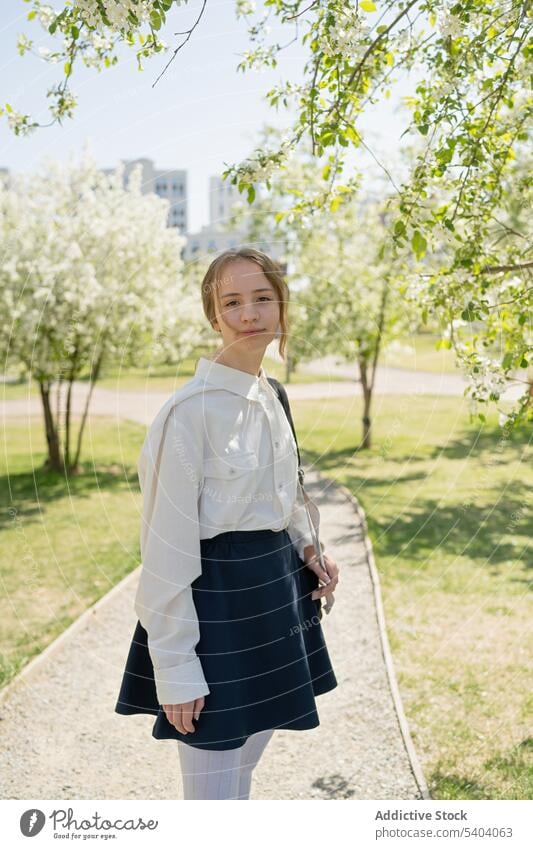 Glückliches junges Mädchen steht im Schatten eines Baumes Jugendlicher Teenager Schüler Park Lächeln Weg positiv Schulmädchen Schule Sommer zurück zur Schule