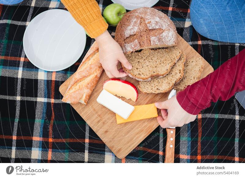 Anonyme Freundinnen beim gemeinsamen Essen auf dem Lande Frauen Picknick Brot Lebensmittel Landschaft essen Käse Schneidebrett Park genießen Rasen