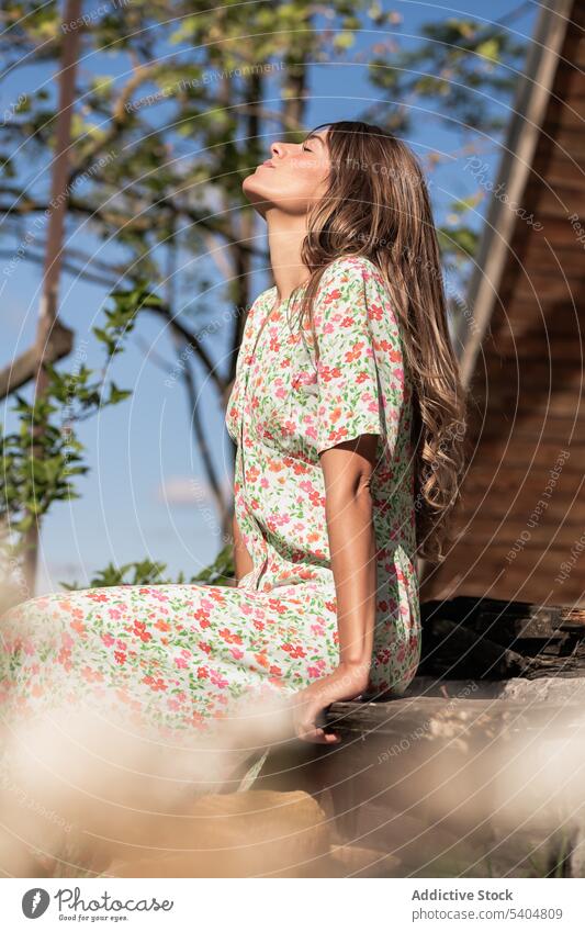 Entspannende Frau auf der Veranda in der Landschaft sitzend Sonnenlicht genießen Sommer Freizeit Windstille Natur sorgenfrei Augen geschlossen Harmonie ruhig