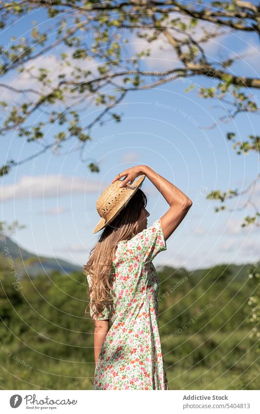 Frau in Sommerkleid und Hut auf dem Lande Sonnenkleid Baum Landschaft romantisch Natur Kleid geblümt Feld ruhig feminin Blütezeit Gelassenheit Stil sorgenfrei