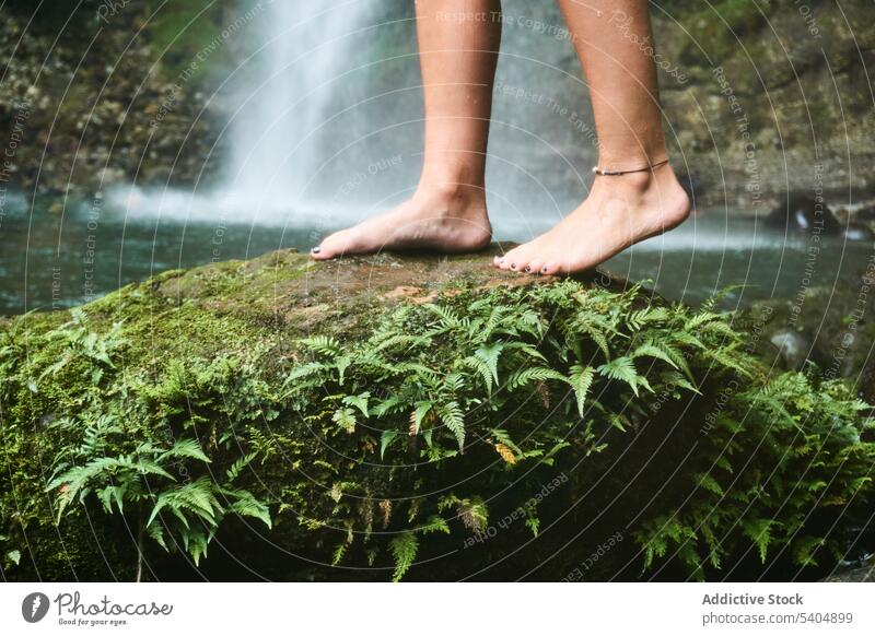 Unbekannte Frau steht auf einem Felsen mit Graspflanzen in der Nähe eines Wasserfalls Reisender Barfuß grün Pflanze Sommer Fußknöchel jung Urlaub Tourismus