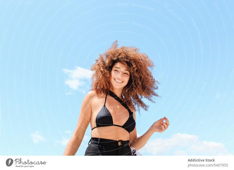 Unbekümmerte ethnische Frau vor blauem Himmel genießen Sommer Sonne sorgenfrei Bikini Top Inhalt sich[Akk] entspannen Afro-Look Frisur Urlaub schlank Shorts