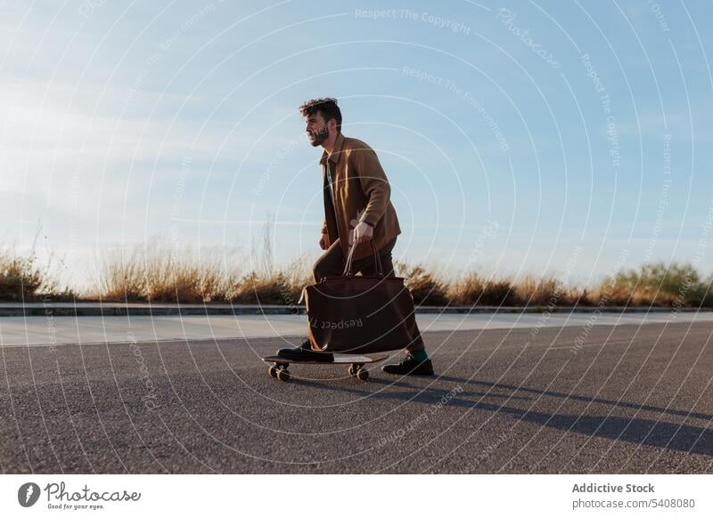 Junger bärtiger Skater mit Tasche fährt auf der Straße Mann Longboard Fähigkeit Mode Stil Skateboard Asphalt Mitfahrgelegenheit Hobby Aktivität männlich