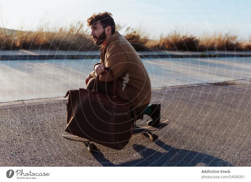 Junger bärtiger Skater mit Tasche fährt auf der Straße Mann Longboard Fähigkeit Mode Stil Skateboard Asphalt Mitfahrgelegenheit Hobby Aktivität männlich