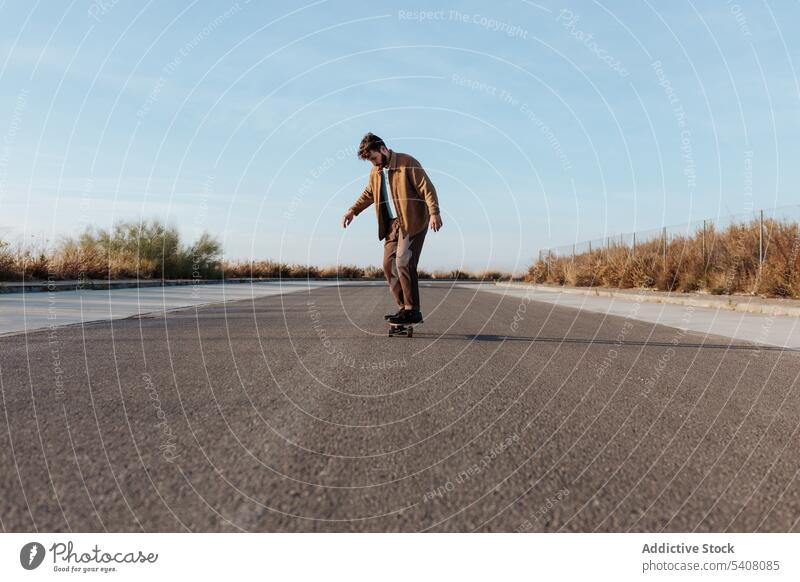 Junger bärtiger Skater auf Asphaltstraße Mann Mitfahrgelegenheit Straße Skateboard Landschaft ländlich Natur Hobby Subkultur üben Fähigkeit männlich Energie