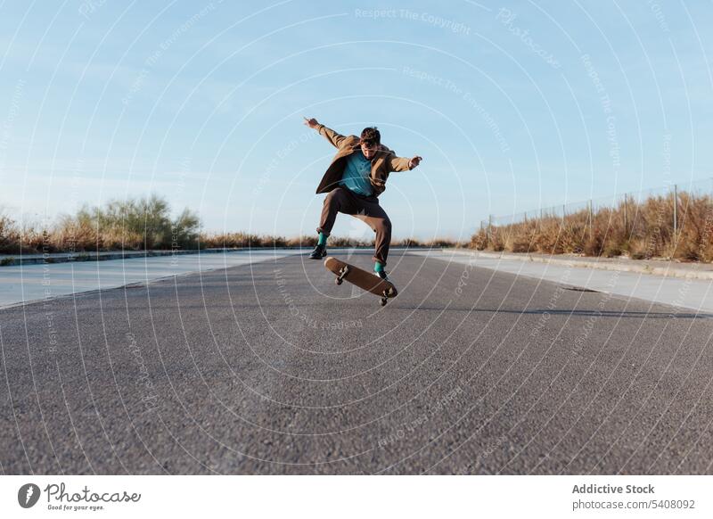 Energetischer junger Skater, der einen Trick auf dem Skateboard vorführt Mann Kickflip springen Stunt Energie Fähigkeit Straße Landschaft Natur ländlich