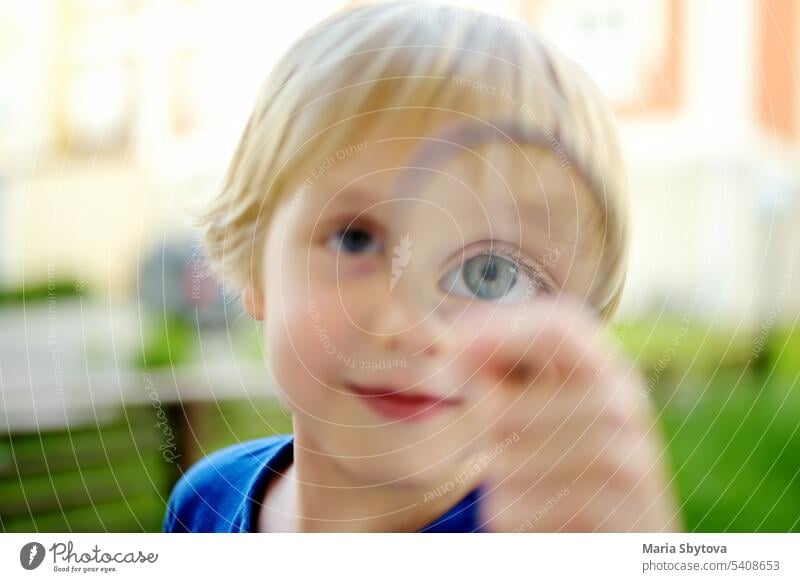 Kleiner Junge spielt mit Lupe. Baby schaut Sie vorsichtig mit der Lupe an. Aktivität für neugieriges Kind. Charmantes Kind erforscht die Natur mit Lupe.