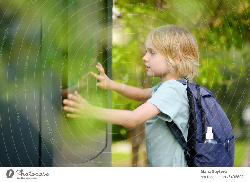 Kleiner Junge Tourist Studium an der großen öffentlichen Outdoor-Straßenkarte der Stadt. Kind berührt Bildschirm und sucht nach dem Weg. Kind interessiert sich für eine visuelle Karte oder Werbeplakate auf der Straße