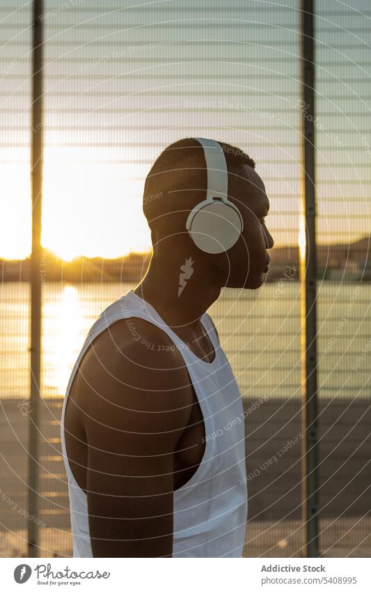 Schwarzer Sportler mit Kopfhörern beim Ausruhen nach dem Training Mann Athlet ernst muskulös sportlich Musik zuhören passen männlich Sportbekleidung Lifestyle