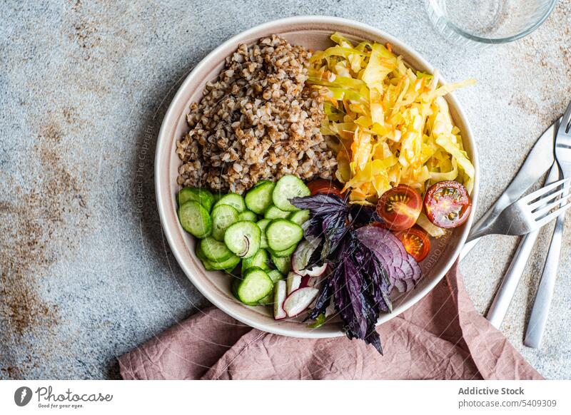 Teller mit leckerem Veggie-Gericht, Besteck und Gläser auf dem Tisch Vegetarier Buchweizen Gemüse Zwiebel Salatgurke Tomate Basilikum Schalen & Schüsseln