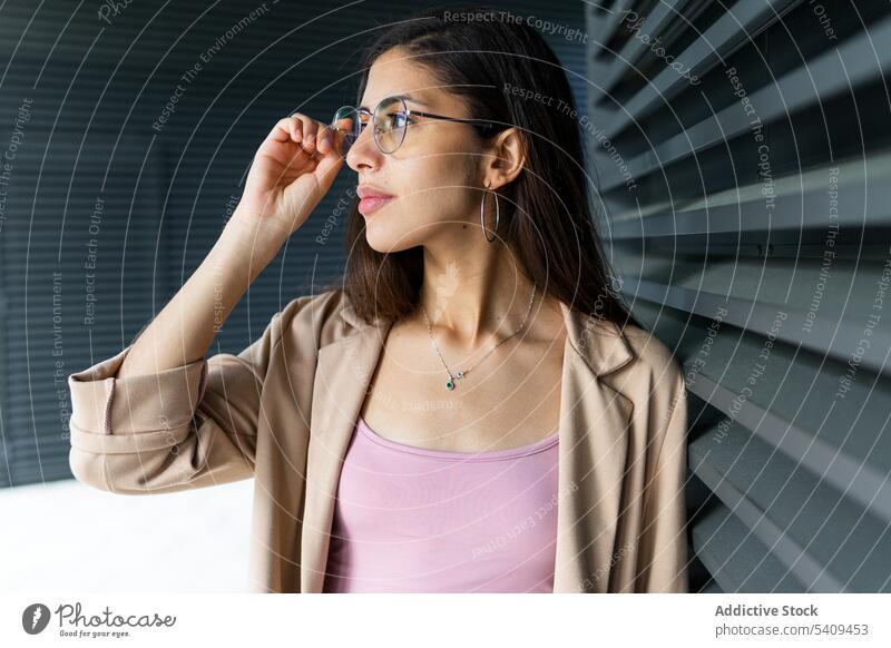 Stilvolle Frau in der Nähe der grauen Wand Geschäftsfrau Unternehmer Haare berühren formal Brille Accessoire Vorschein Business Outfit nahöstlich professionell