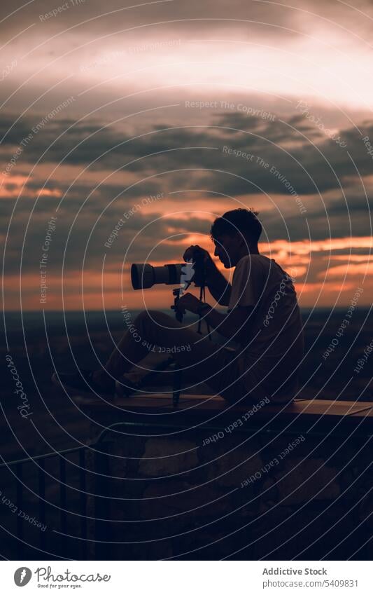 Unbekannter Mann mit Kamera, der den orangefarbenen Abendhimmel mit schwarzen Wolken fotografiert fotografieren Fotokamera Sonnenuntergang Himmel Natur Cloud