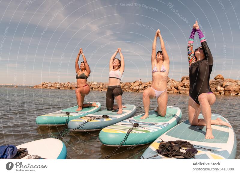 Gruppe von Frauen, die Yoga in der Haltung des Kriegers 1 machen Strand Dehnung üben Gleichgewicht Krieger-Pose Übung Aktivität Küste knien positionieren