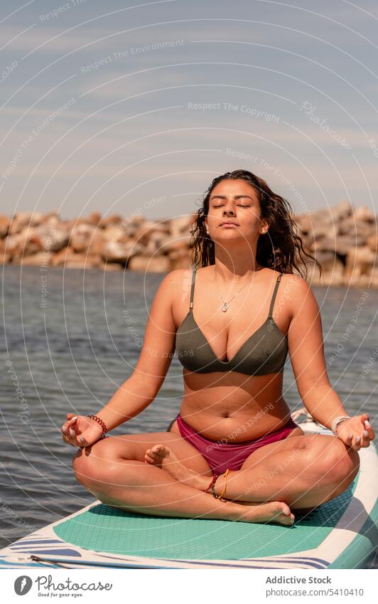 Schlanke Frau im Bikini meditiert auf einem Paddleboard im Meer Sup-Yoga Paddelbrett gyan mudra Zusatzplatine meditieren Gleichgewicht Zen Seeküste Mudra üben