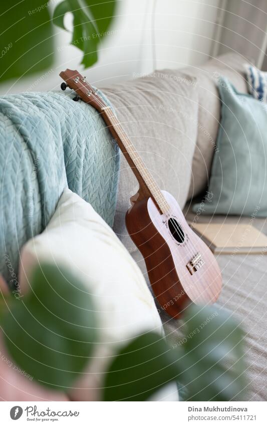 Ukulele-Instrument, Bücher und Kissen auf der Couch. Gemütliche trendige Hipster-Wohnung Innenarchitektur.  Konzept des langsamen Lebens. Seitenansicht.