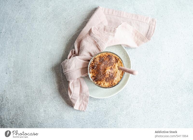 Glasbecher mit Kaffeesahne-Dessert mit Schokoladenpulver und Eis Tasse Becher Pulver Löffel Teller Serviette Tisch Oberfläche grau verschwommener Hintergrund