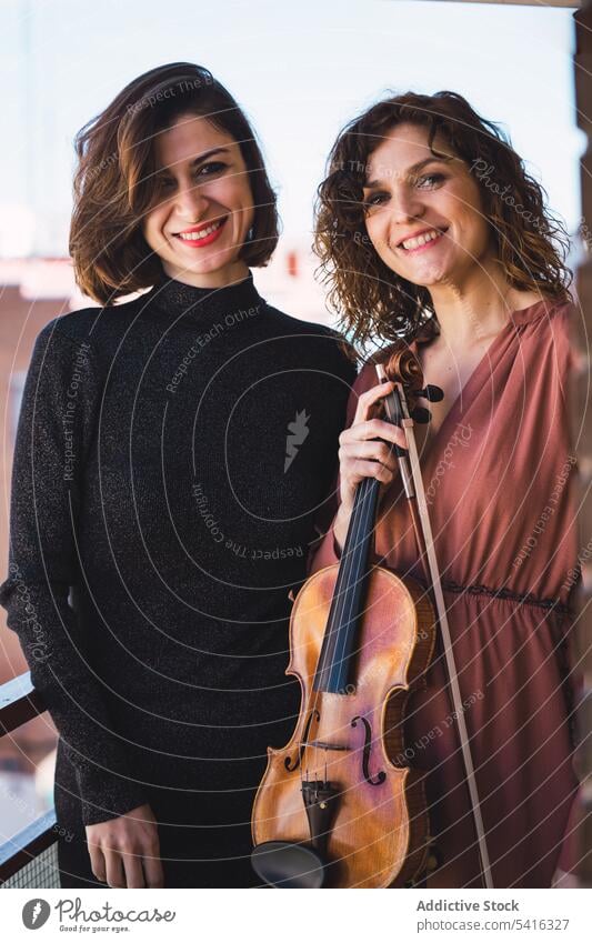 Junge lächelnde Frauen mit Geige auf Balkon Musiker jung Lächeln elegant Freund Instrument heiter Kunst Klang Spielen Leistung Melodie Geiger Klassik schön